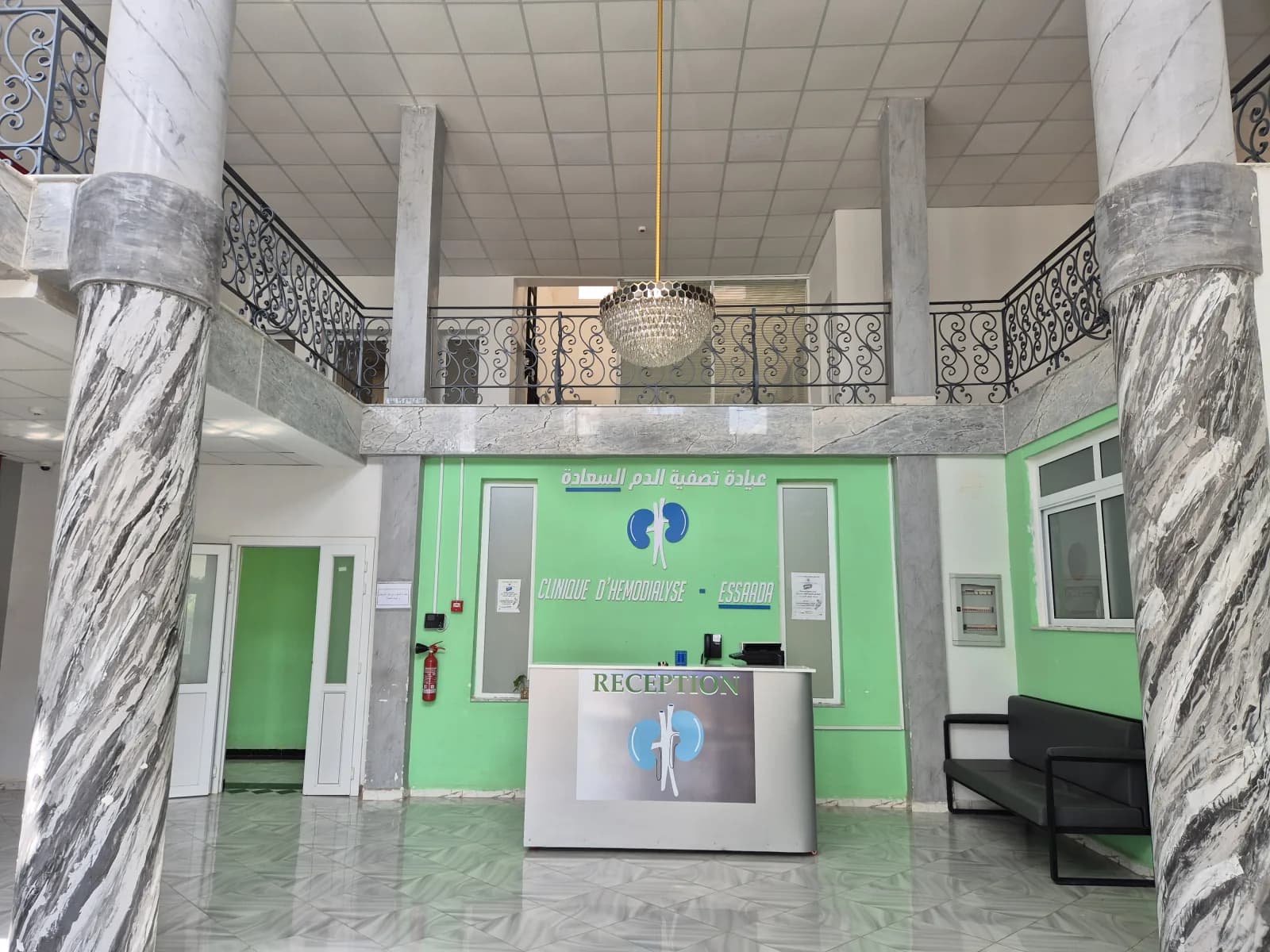 Hall d'accueil de la Clinique d'Hémodialyse ESSAADA à Sidi Bel Abbès — piliers en marbre, comptoir de réception et escalier monumental