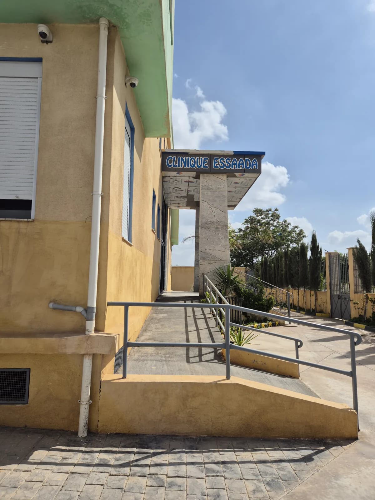 Façade extérieure de la Clinique ESSAADA à Sidi Bel Abbès — enseigne « CLINIQUE ESSAADA », rampe d'accès patients et entrée principale