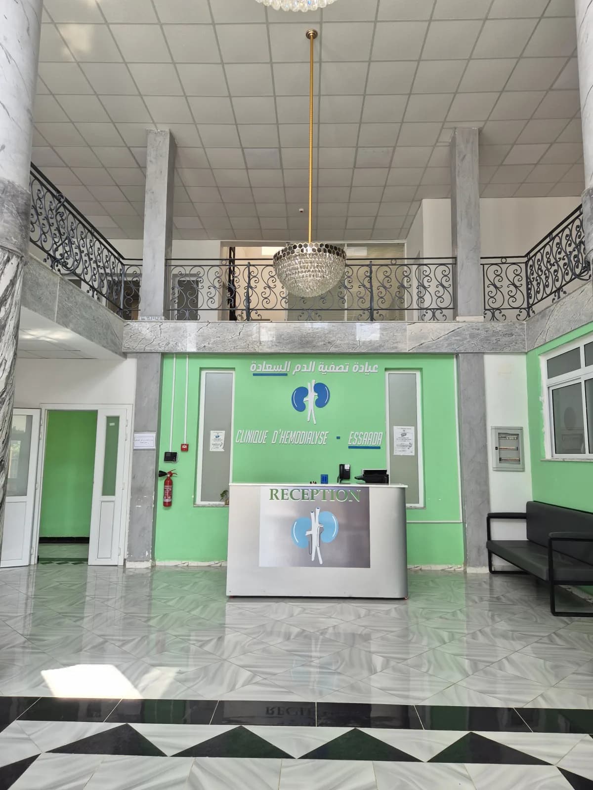 Comptoir de réception de la Clinique d'Hémodialyse ESSAADA à Sidi Bel Abbès — logo (rein stylisé) et signalétique bilingue français-arabe pour l'accueil des patients