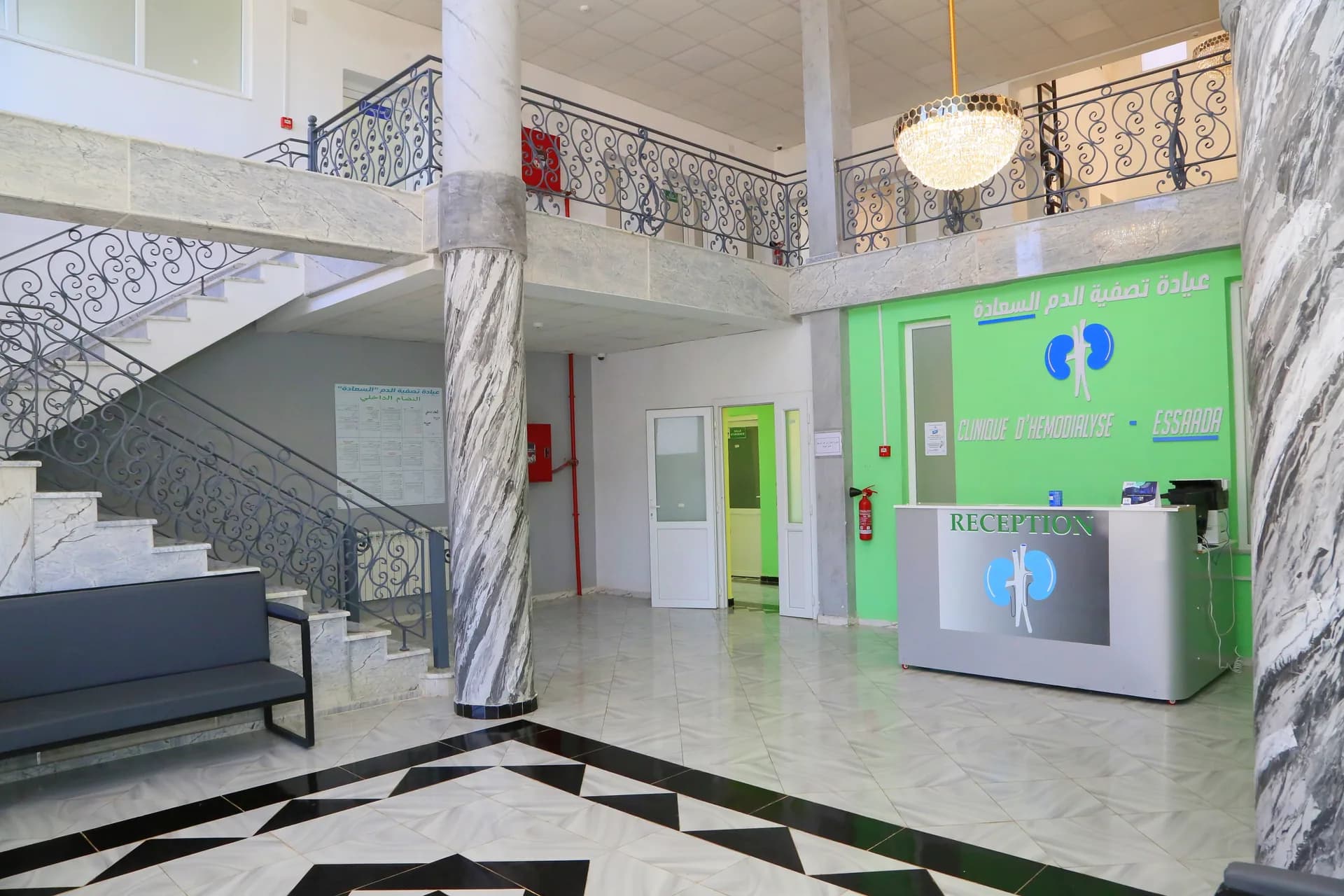Hall d'accueil de la Clinique ESSAADA avec comptoir de réception, escaliers en marbre et lustre